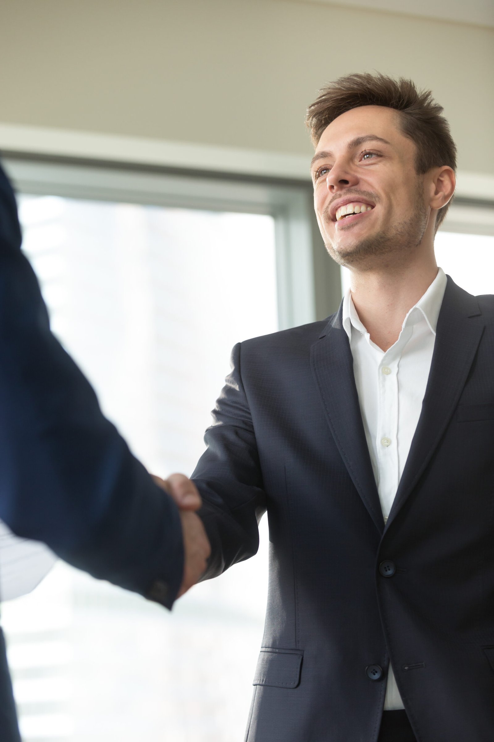 smiling young businessman wearing black suit shaking male hand,